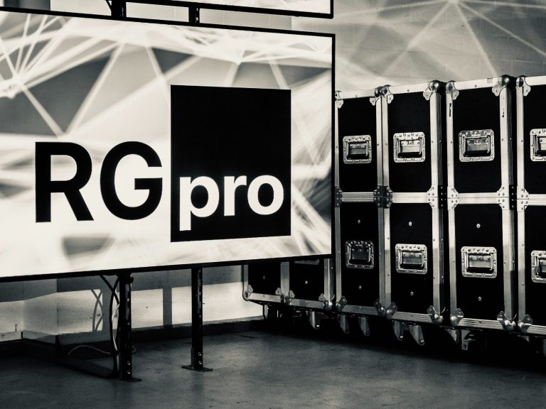 RGpro Image-Motiv Logo von RG pro auf einem Bildschirm, umgeben von transportfertigen Kisten.