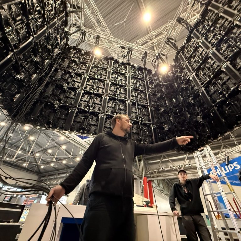 Techniker zeigt auf große, komplexe Bühne mit vielen schwarzen Panels im Hintergrund.