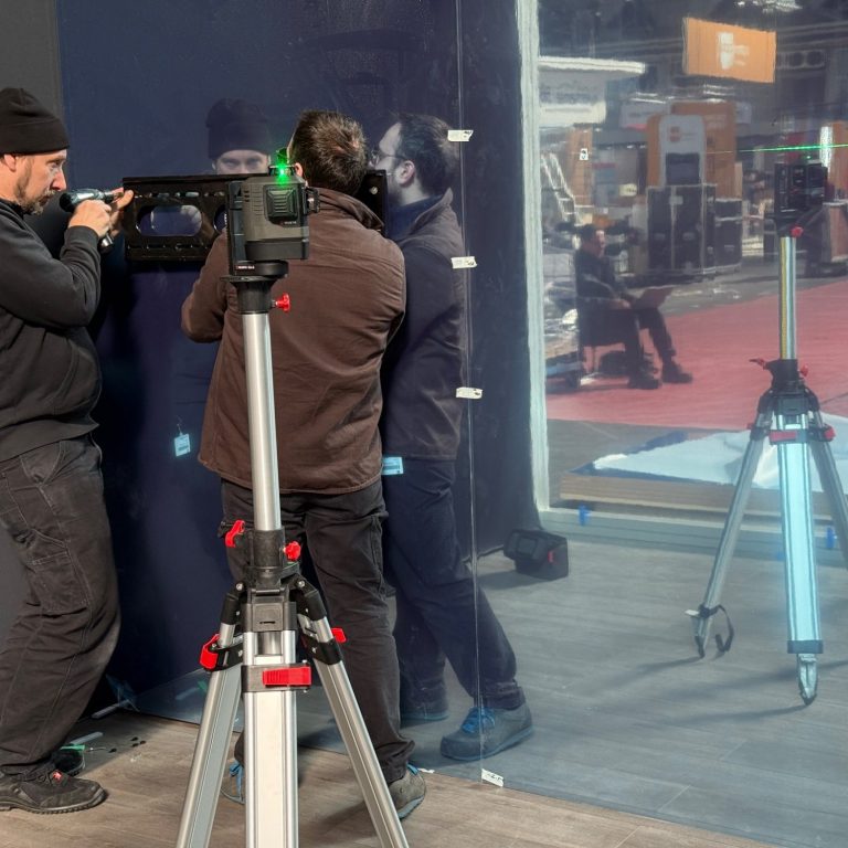 Techniker bei der Installation von Video- und Medientechnik auf einer Messe Zwei Personen montieren eine transparente Wand, im Hintergrund anderer Messeaufbau zu sehen.