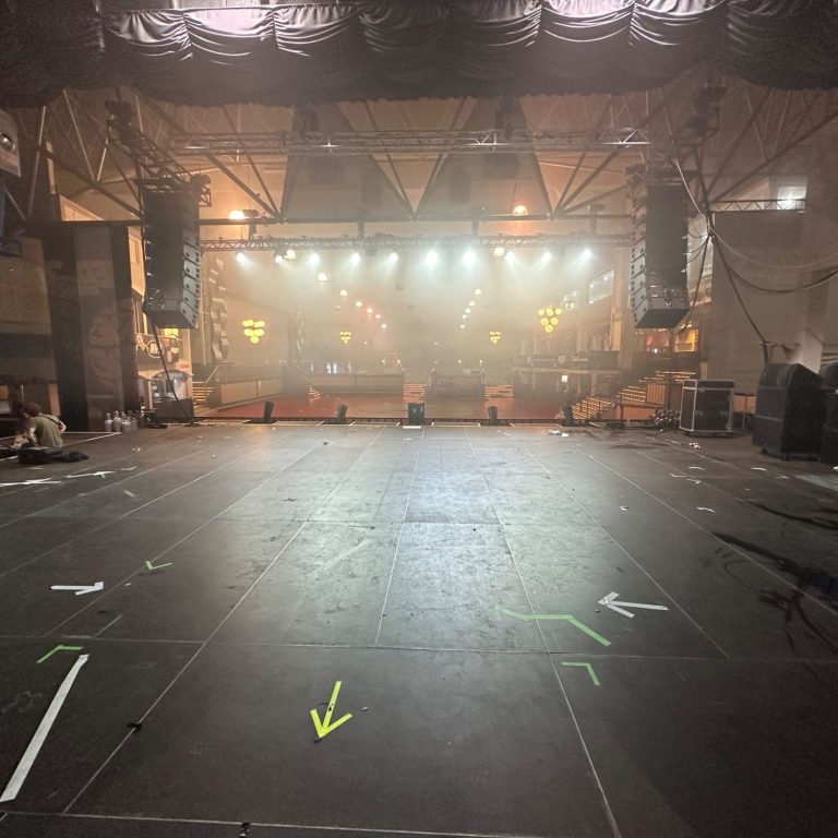 Bühnenaufbau mit professioneller Licht- und Tontechnik für eine Veranstaltung Leere Bühnenfläche in einem Nebel mit Scheinwerferlichtern im Hintergrund.