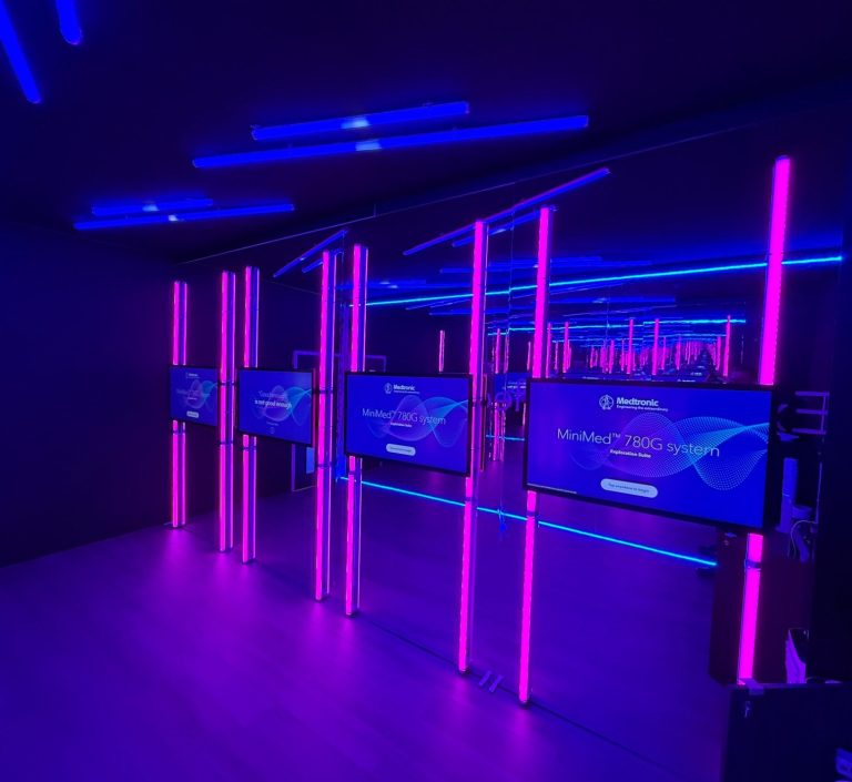 Digitale Medieninstallation mit LED-Licht und Displays für Ausstellung oder Event Dunkler Raum mit neonblauen und pinken Lichtern und mehreren Bildschirmen.
