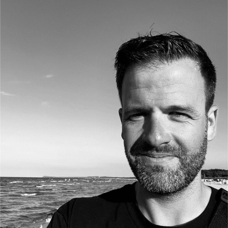 RGpro Geschäftsführer Fabian Richter Portrait eines Mannes am Strand, mit Wasser im Hintergrund und klaren Himmel.